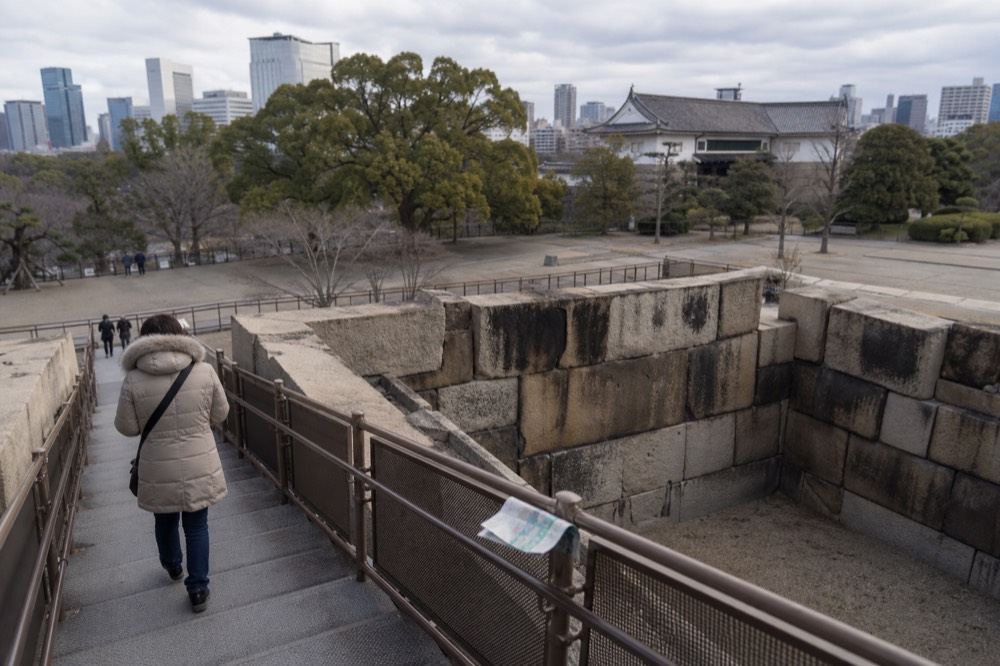 Visitor descending the walkway beside exposed stone wall foundations