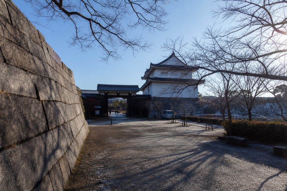 Clear winter sky over the Osaka Castle tower and stone walls, with bare trees and long shadows on the plaza