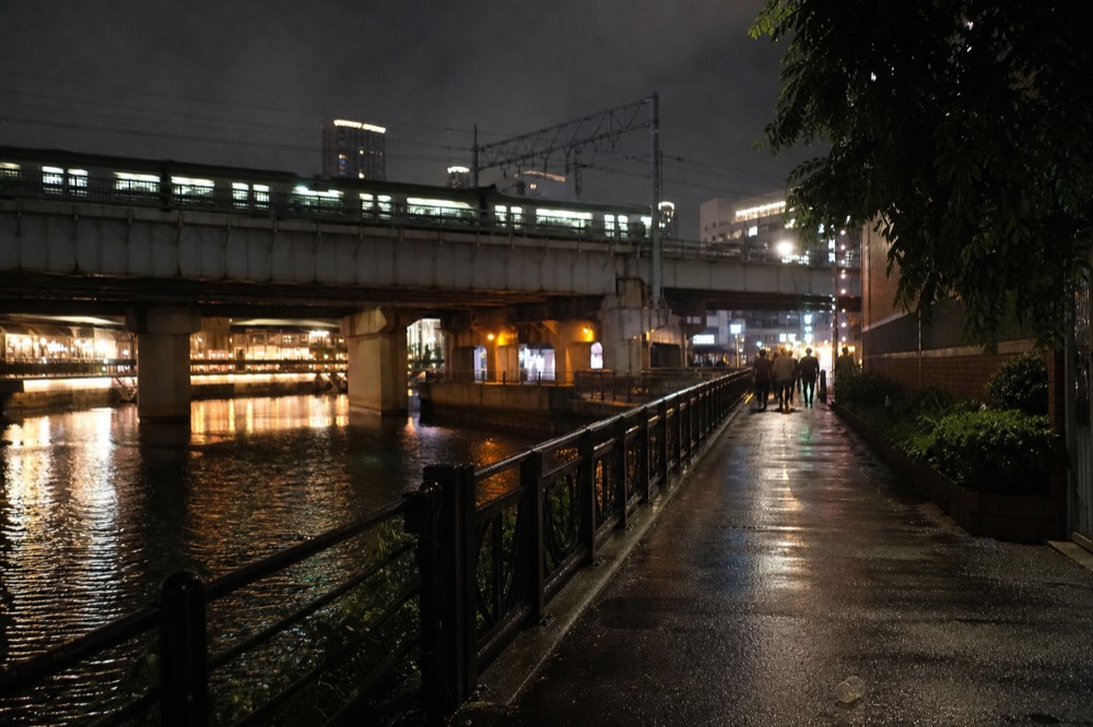A bright Osaka street at night with neon signs and a rail bridge above