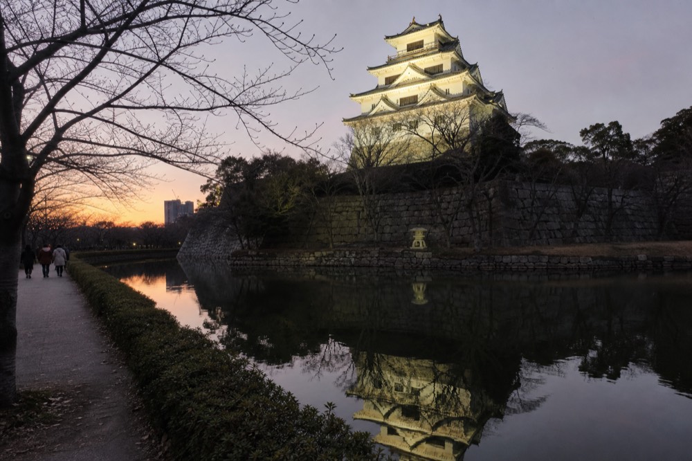 The floodlit white walls of a castle keep reflected in an inner moat at dusk