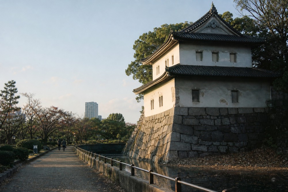 A historic wooden turret with white plaster walls and dark roof tiles beside a stone wall and moat
