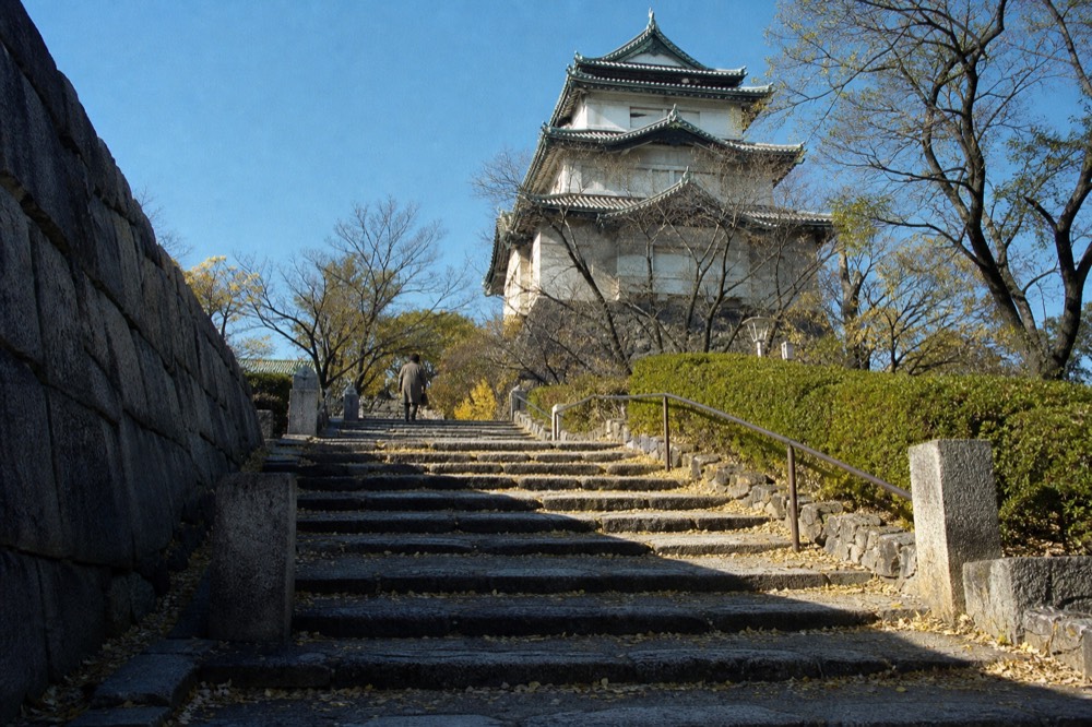 A modern concrete and white-plaster castle tower with green curved roof tiles under a blue sky