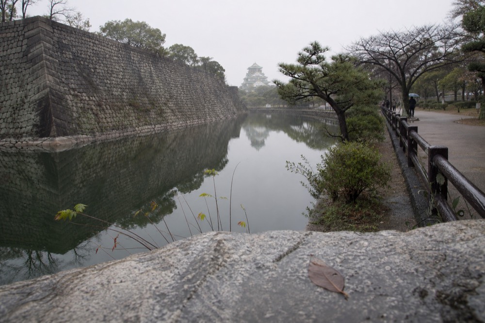 The outer moat and stone wall of Osaka Castle with the tower visible in the distance