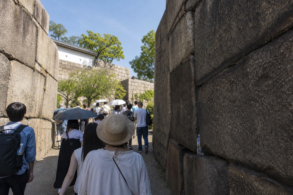 Visitors walking through a stone gate passage of Osaka Castle with high granite walls on both sides