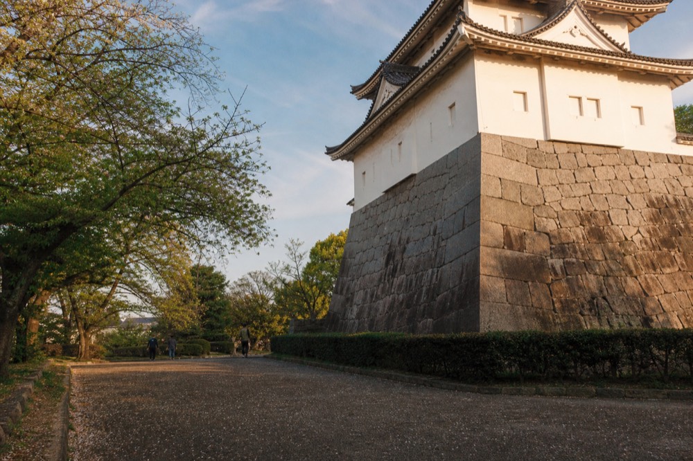 A stone turret with white plastered walls above a stone wall beside a garden path