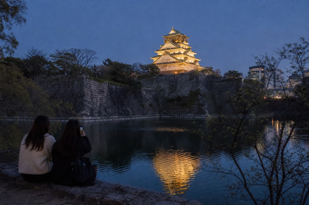The illuminated tower seen from the south side of the outer moat, with the dark water reflecting the golden light
