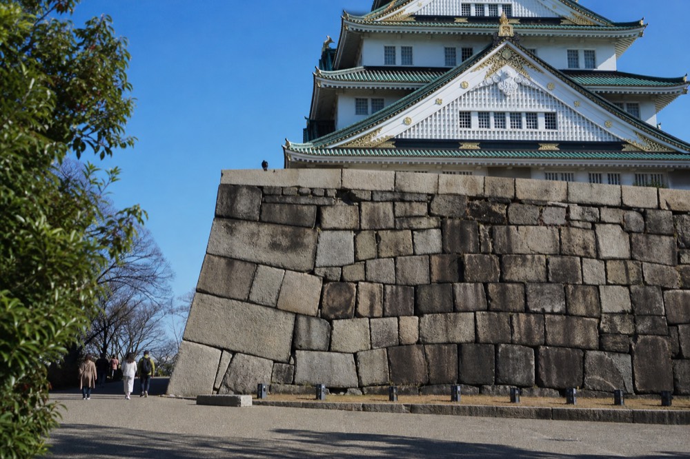 Sunlight falling on the Osaka Castle Main Tower with the stone base and a clear blue sky