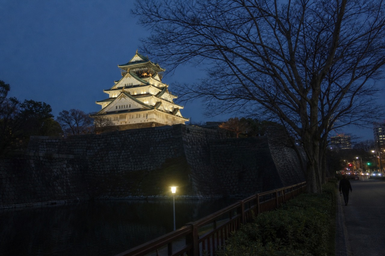 Osaka Castle Main Tower illuminated at dusk with stone walls and moat in the foreground