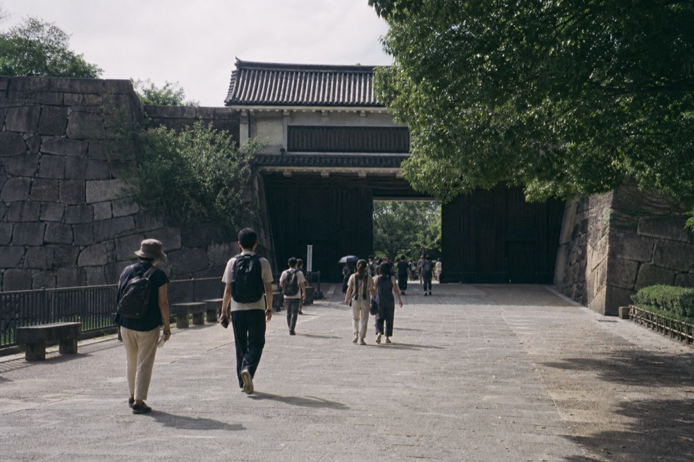 Visitors walking along a stone path toward a castle gate among trees