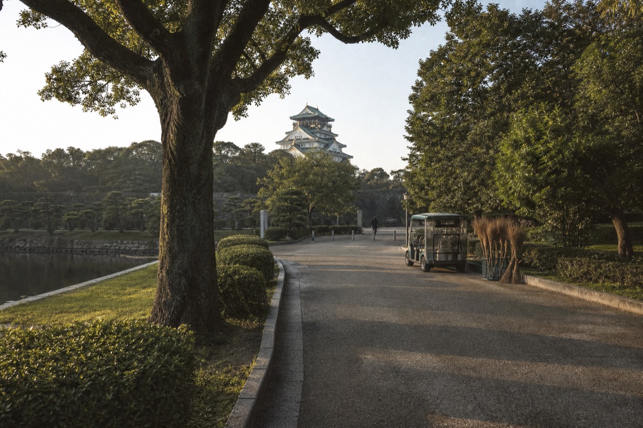 Osaka Castle Main Tower rising above the moat and tree-lined park paths in morning light